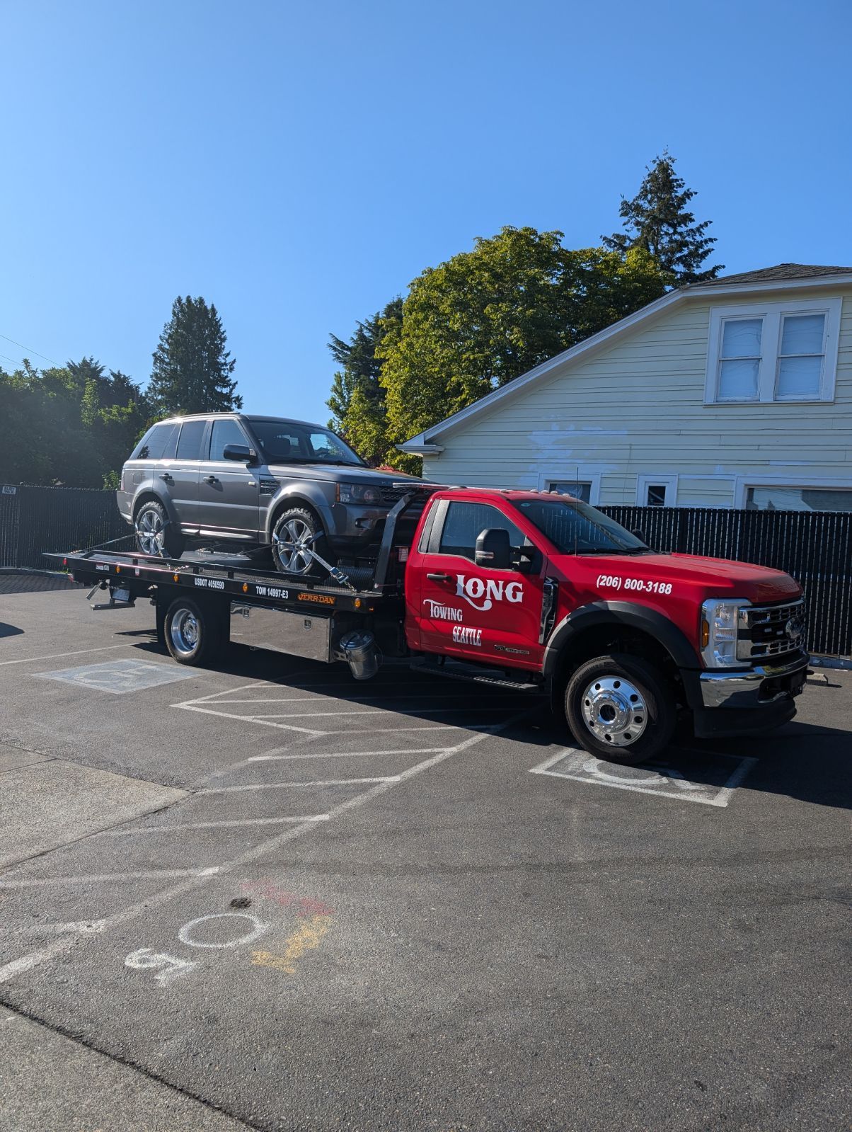 A red tow truck is towing a silver suv in a parking lot.