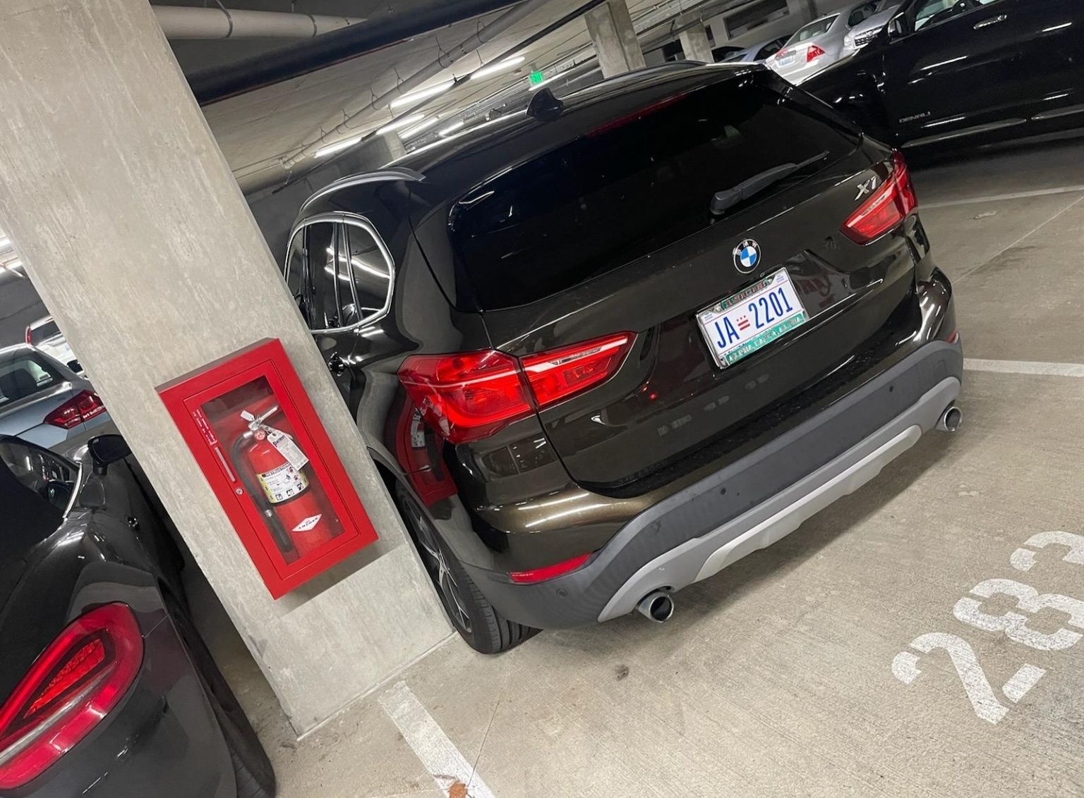A black bmw is parked in a parking garage next to a fire extinguisher.