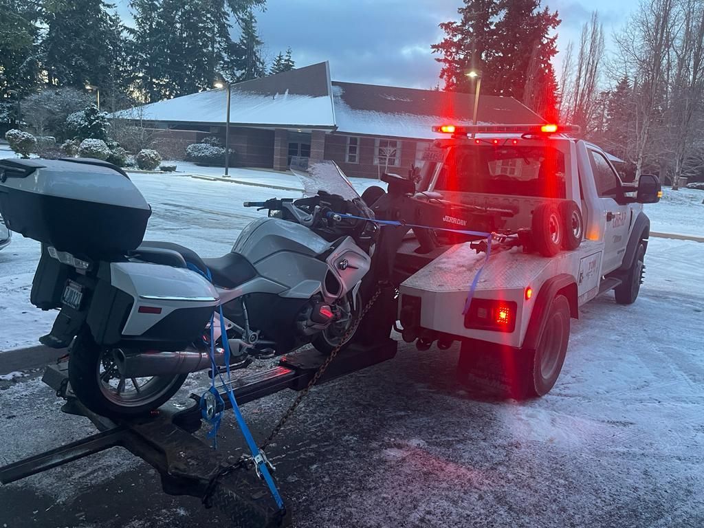 A tow truck is towing a motorcycle in the snow.