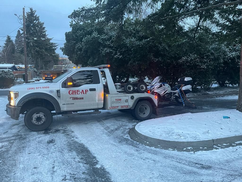A tow truck is towing a motorcycle in the snow.