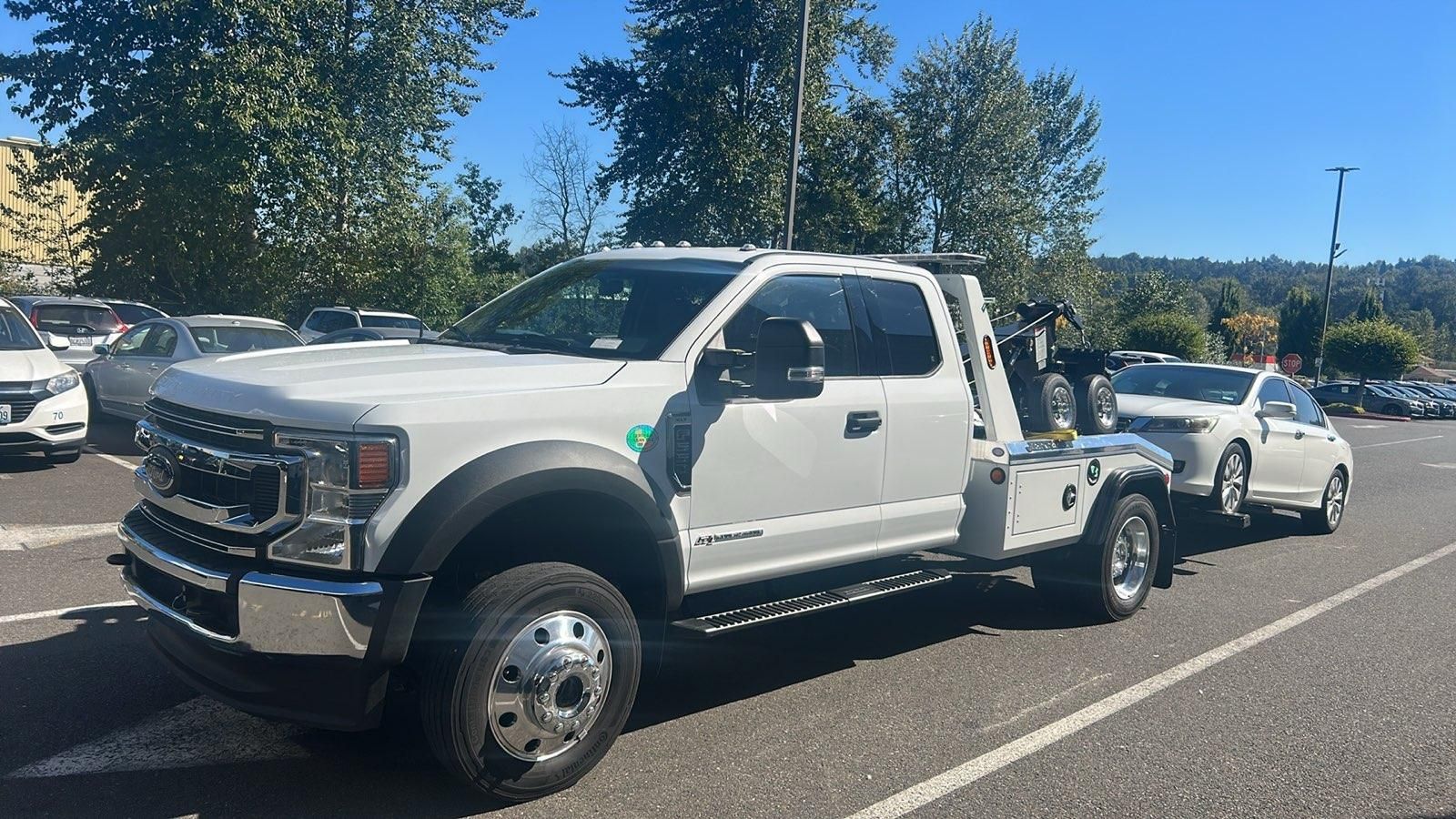 A white tow truck is towing a white car in a parking lot.