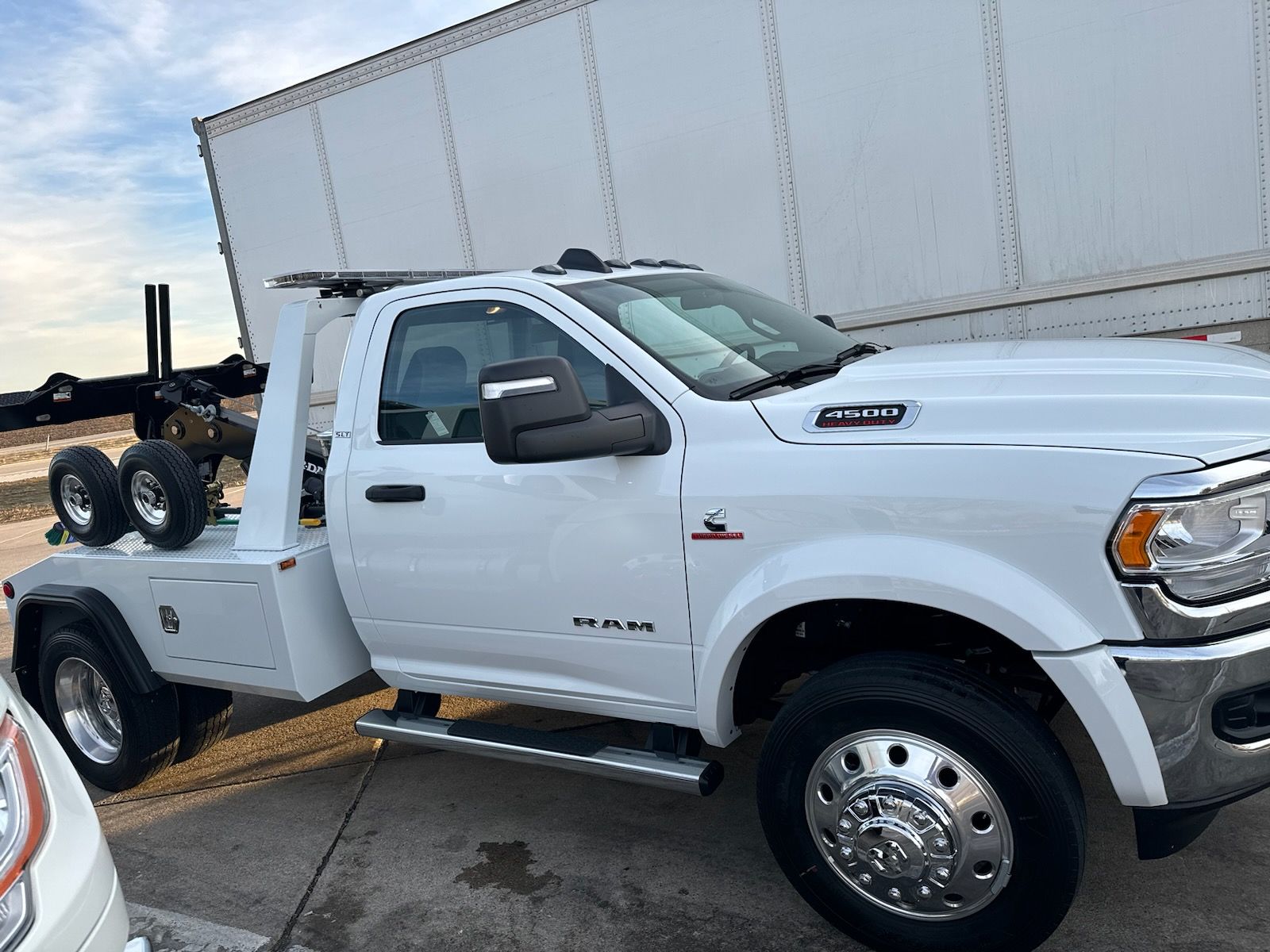 A white tow truck is parked in front of a white truck.