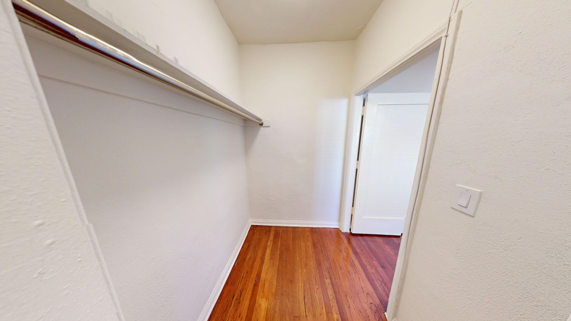 Empty closet with wooden floor, white walls, and a doorway.