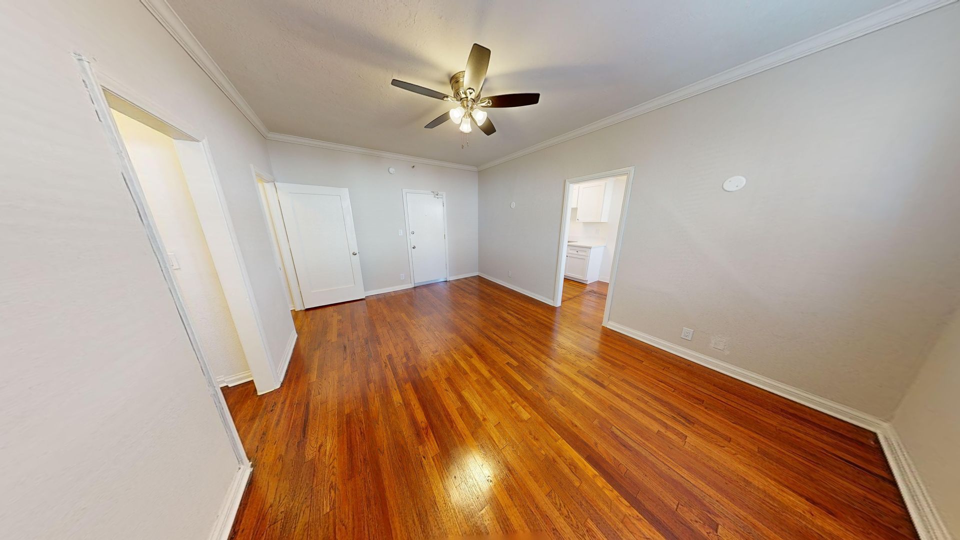 Empty room with hardwood floors, white walls, and a ceiling fan.