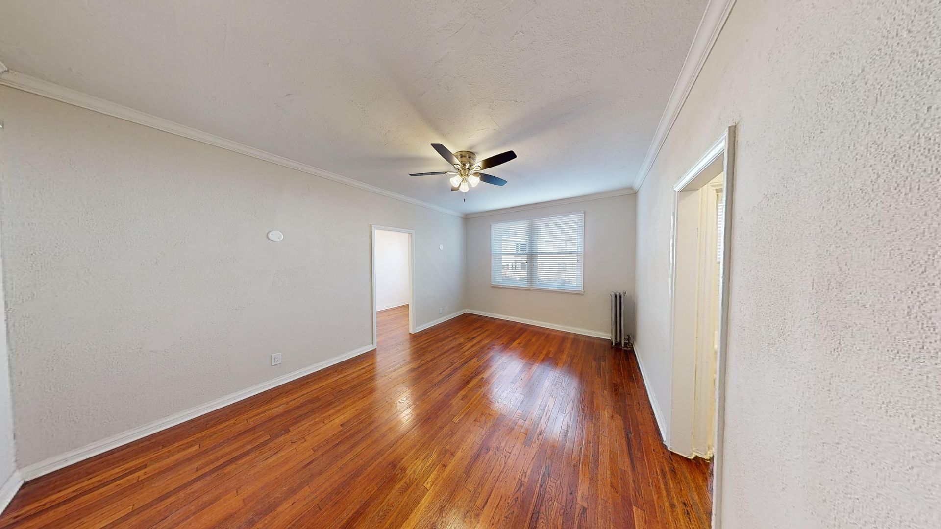 Empty room with wood floors, white walls, and a ceiling fan.