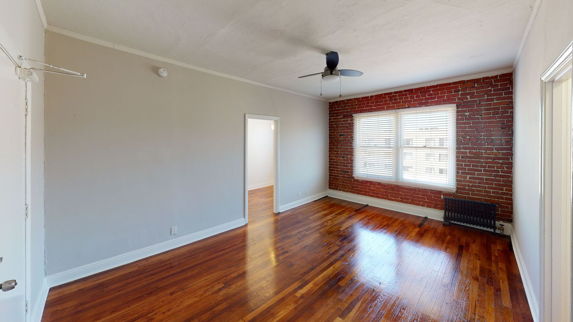 Empty room with hardwood floors, brick accent wall, white walls, and a window.