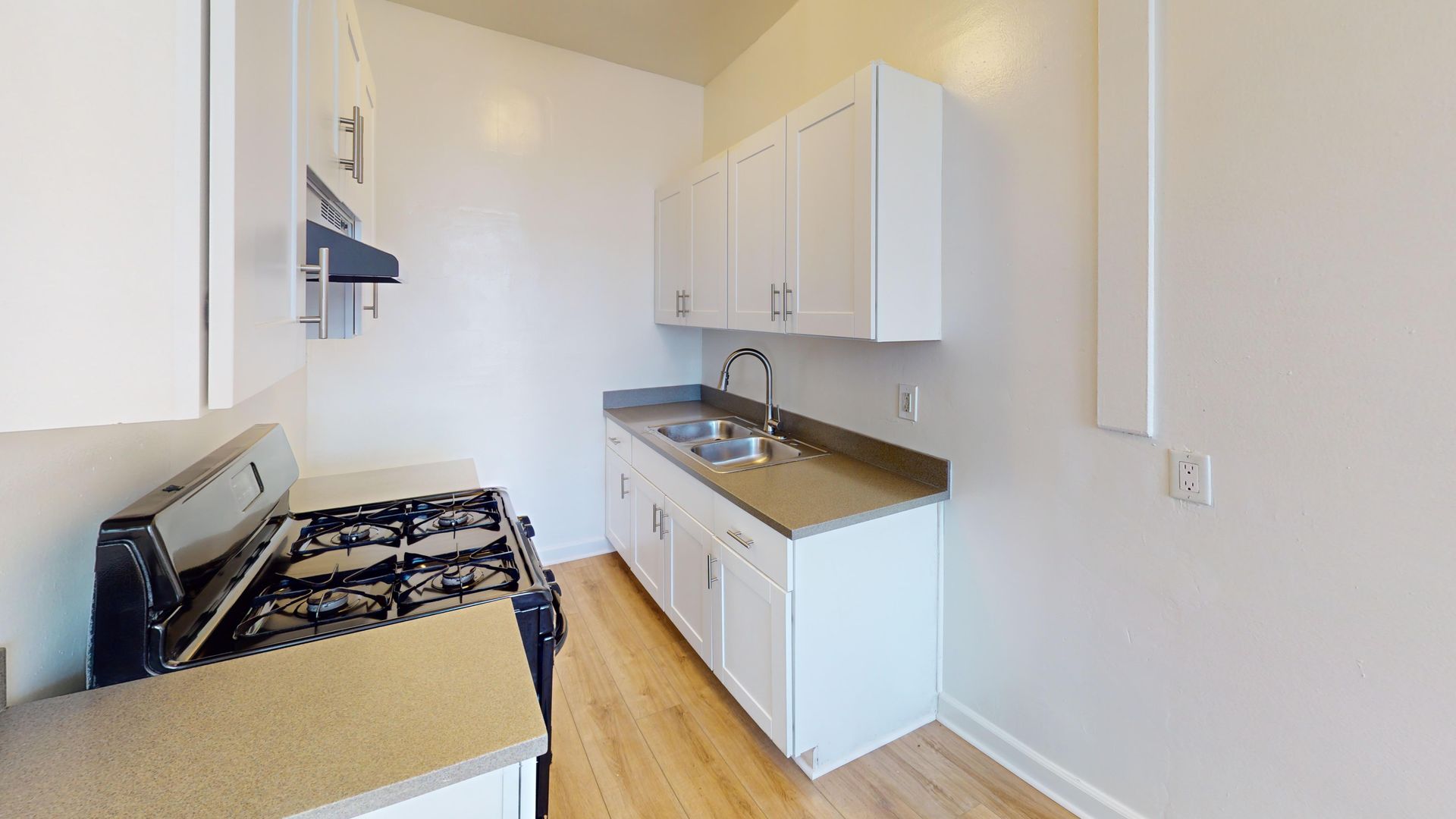 Kitchen with white cabinets, light countertops, gas stove, and stainless steel sink.