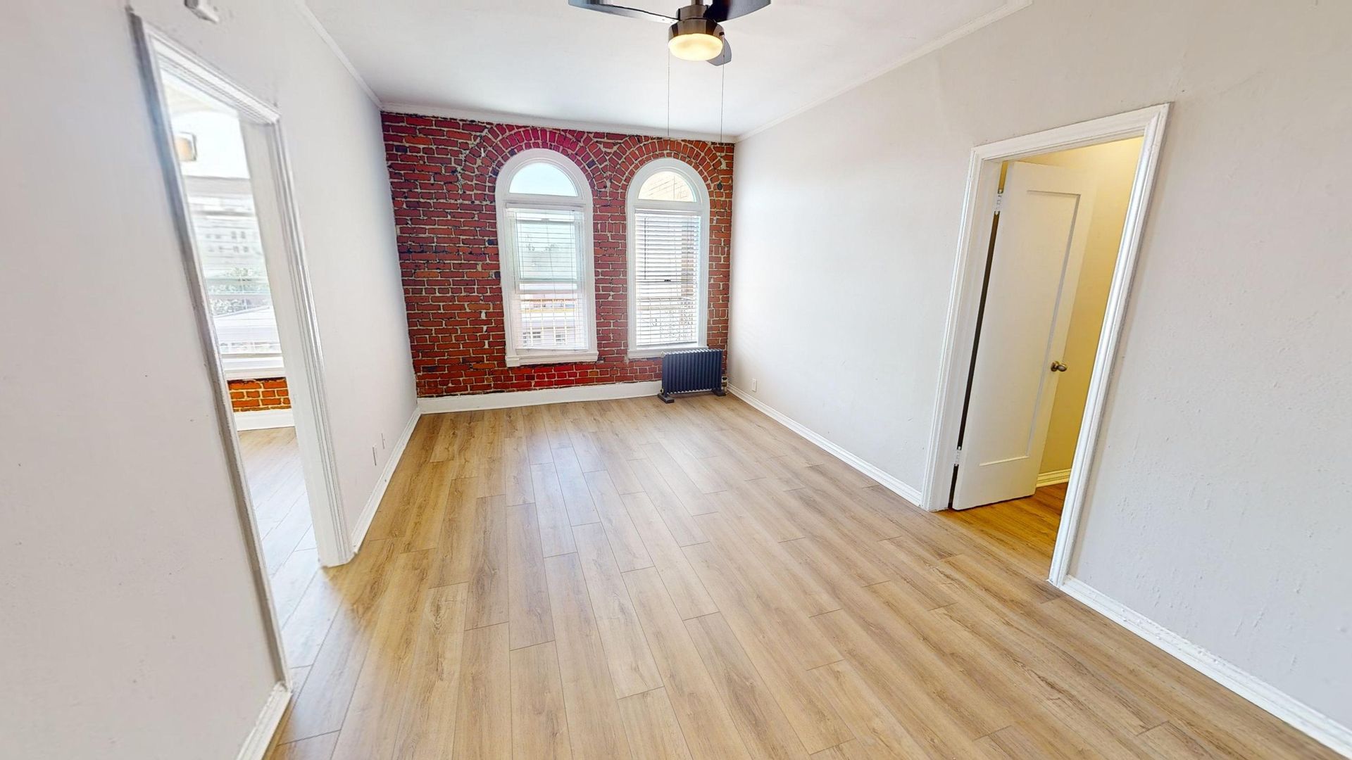 Empty room with brick wall and arched windows, hardwood floors, and doorways.