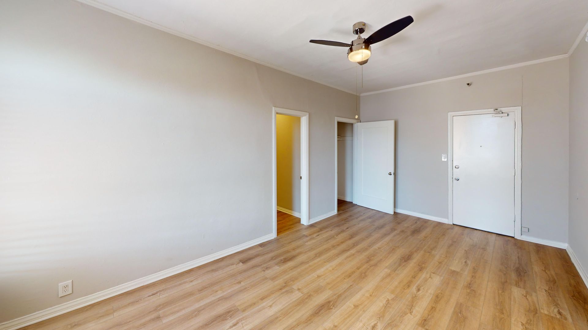 Empty room with light wood flooring, white trim, gray walls, and open doors.