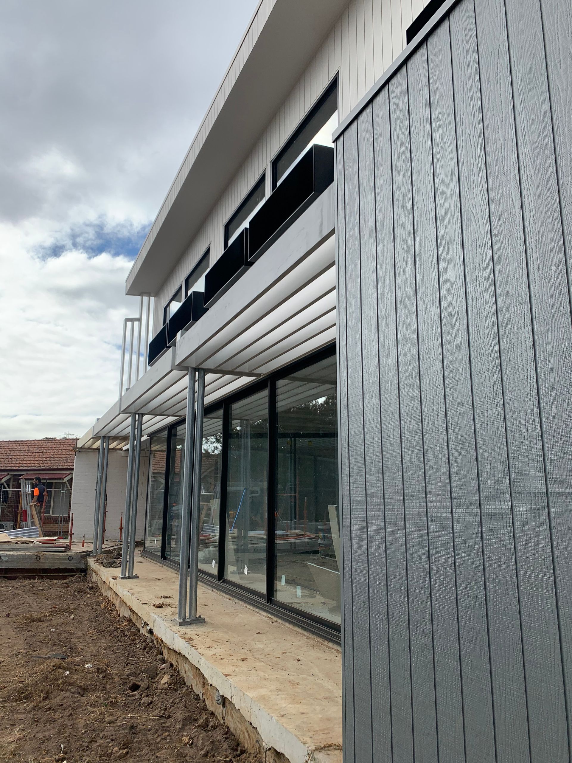 A Man Is Standing In Front Of A Building Under Construction — KM Custom Homes In Mount Eliza, VIC