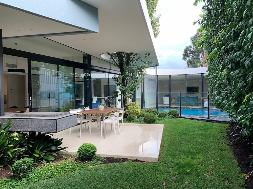 A Patio With A Table And Chairs In Front Of A House With A Pool — KM Custom Homes In Mount Eliza, VIC