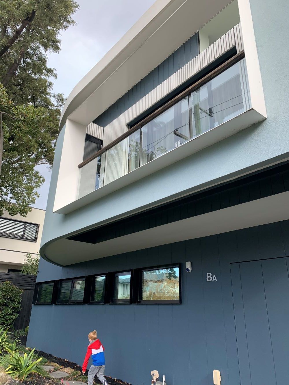 A Little Boy Is Standing In Front Of A Blue Building — KM Custom Homes In Mount Eliza, VIC