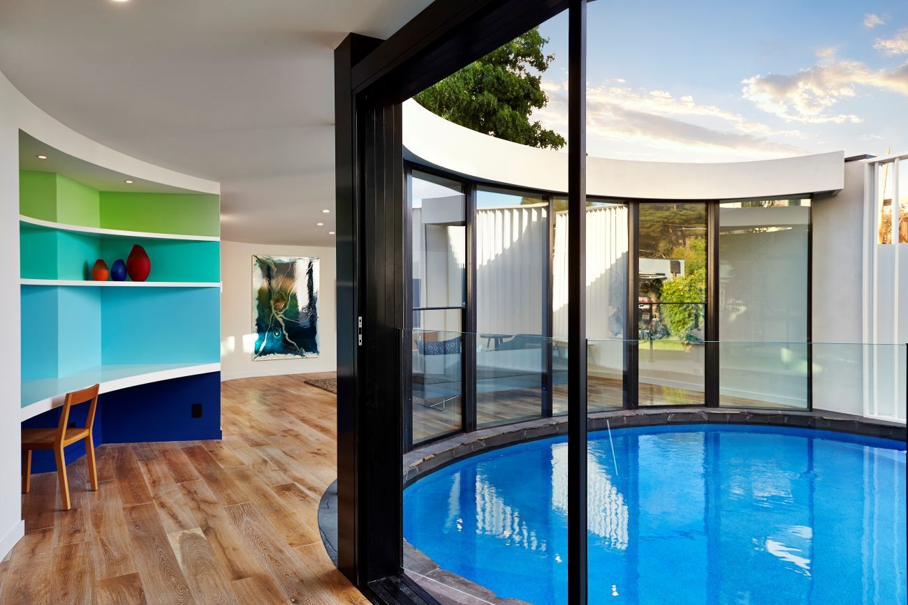 A Large Swimming Pool is Surrounded by a Glass Wall — KM Custom Homes In Mount Eliza, VIC