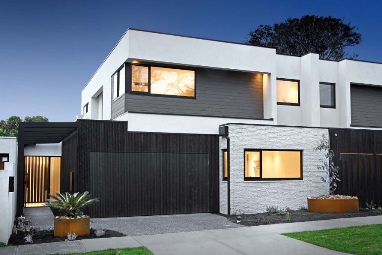 A Modern House With a Black Garage Door is Lit Up at Night — KM Custom Homes In Mount Eliza, VIC