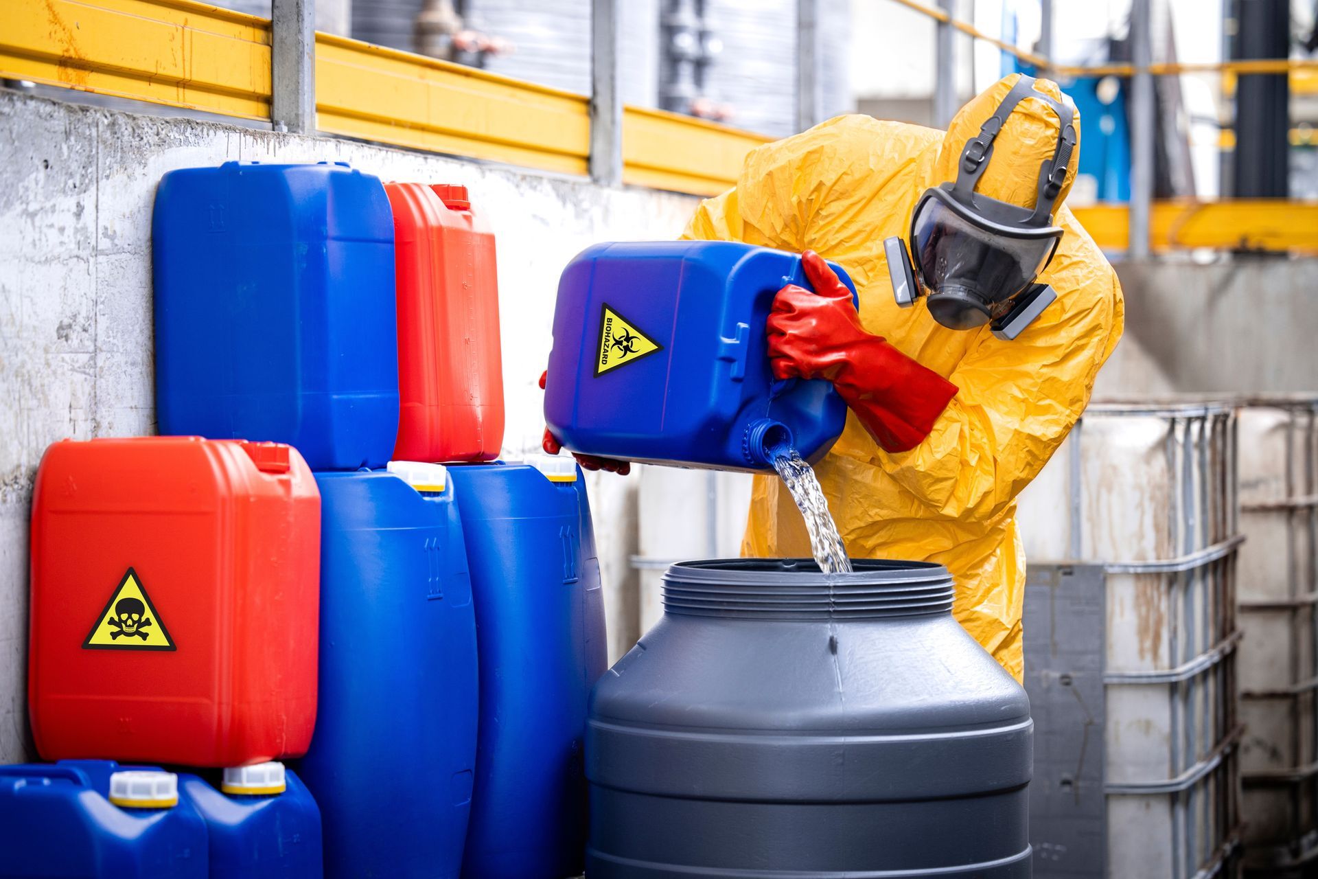 A man in a protective suit is pouring chemicals into a barrel.