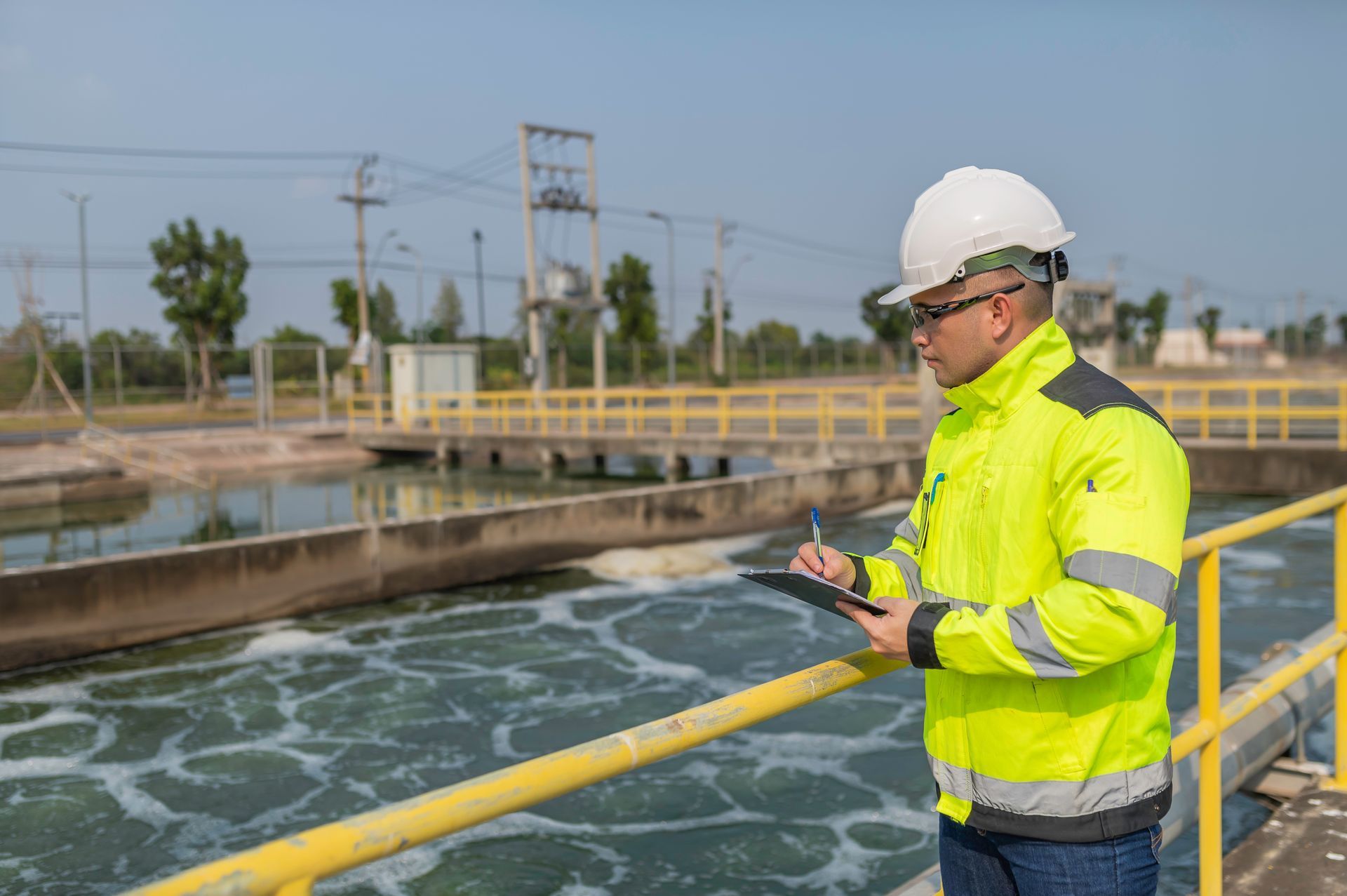 A man in a yellow jacket is standing next to a water treatment plant.