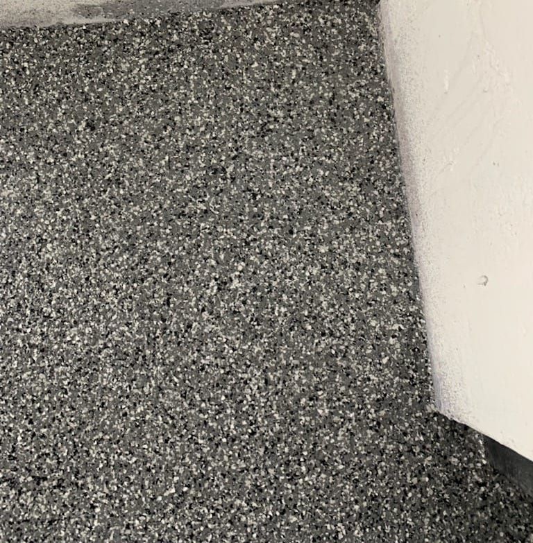 A close up of a gray carpet with a white wall in the background.