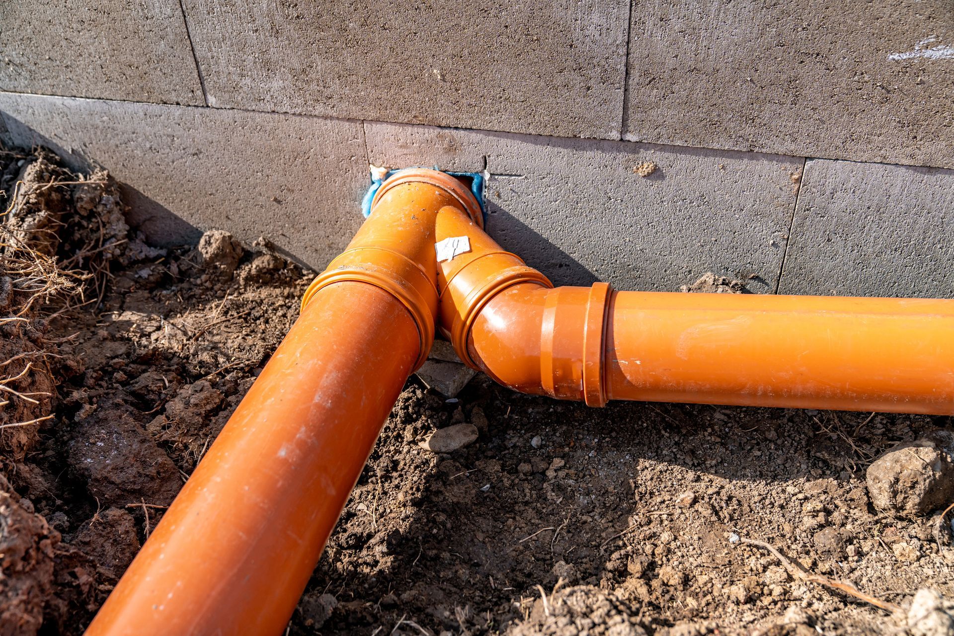 Two orange pipes are connected to each other in the dirt.