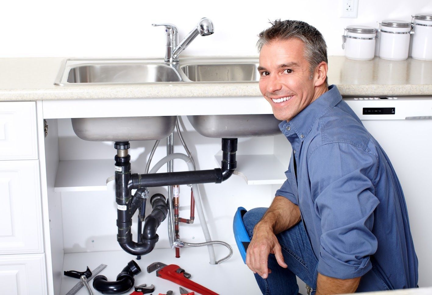 A plumber is fixing a sink in a kitchen.