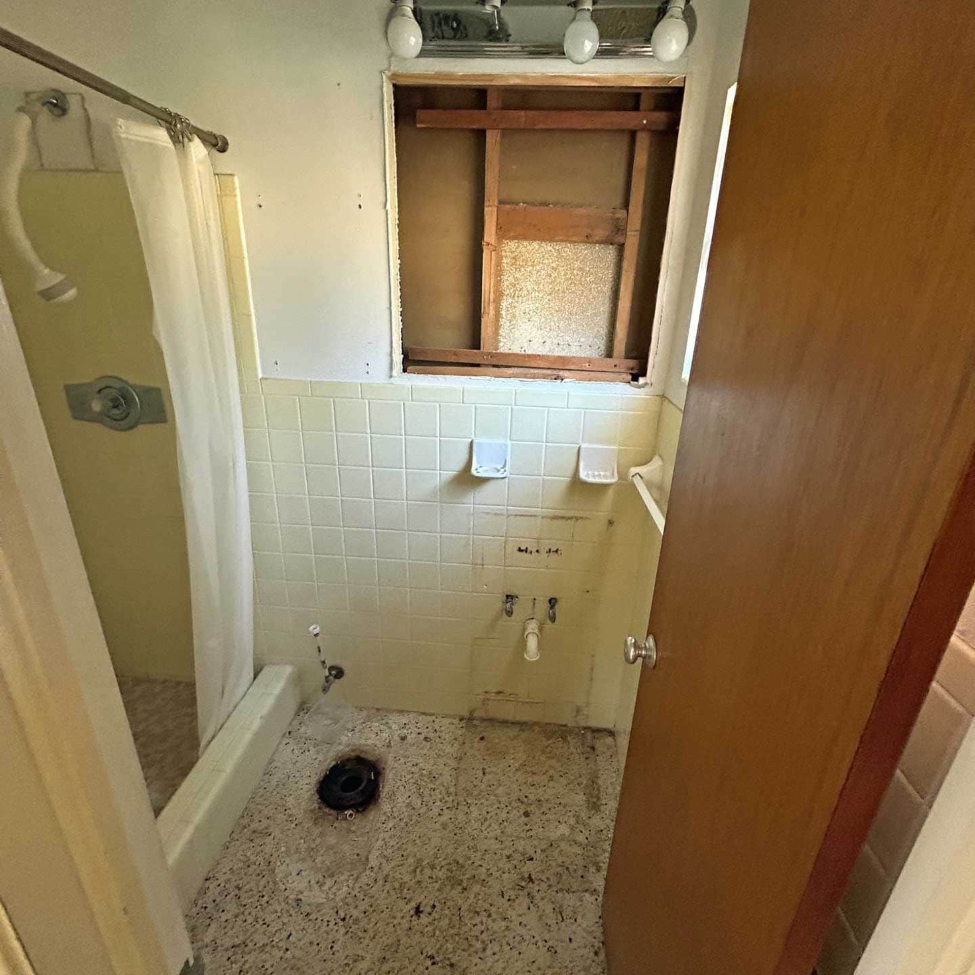 Bathroom interior with a shower, toilet drain, and exposed wall. Door on the right.