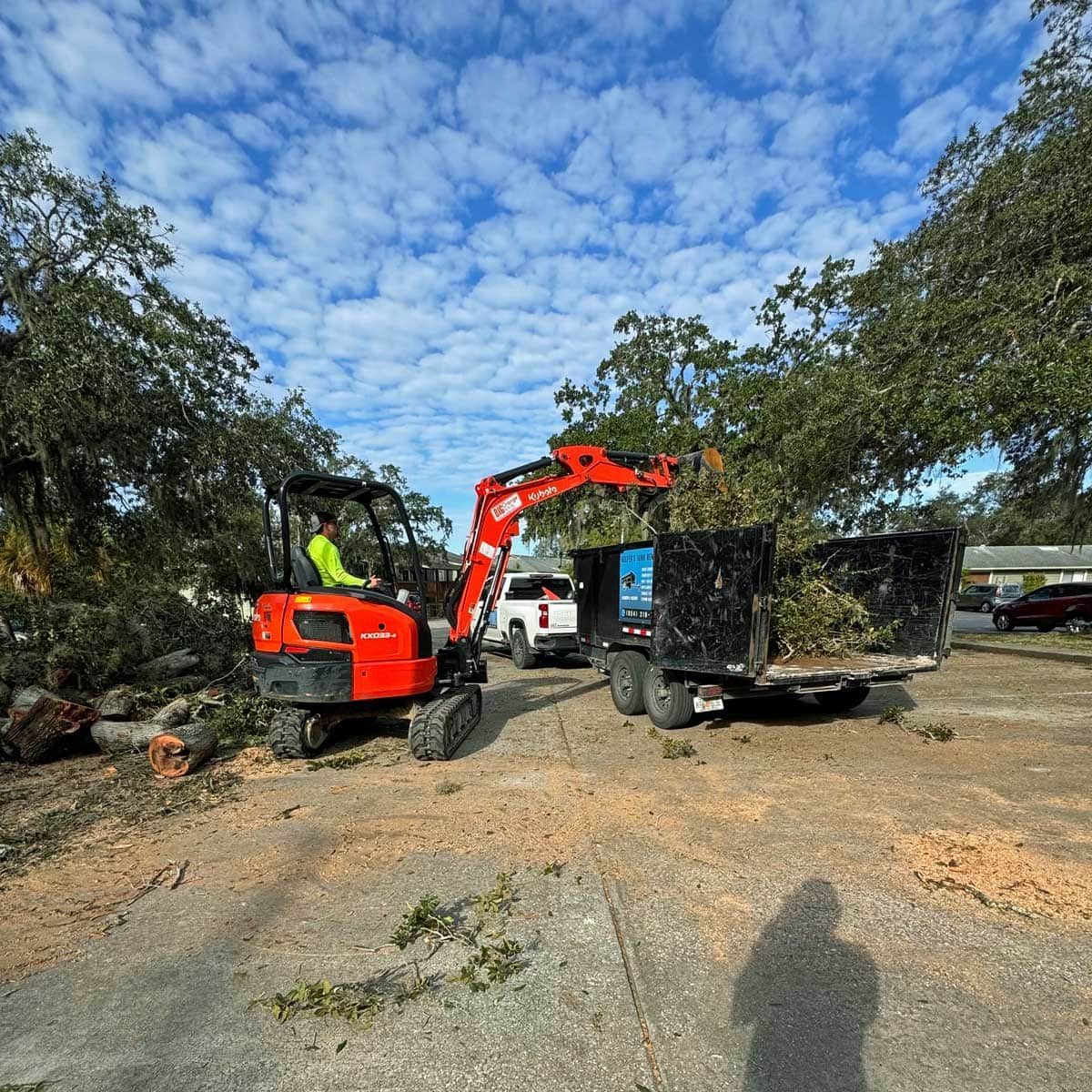 A man is driving a small orange excavator in a parking lot.