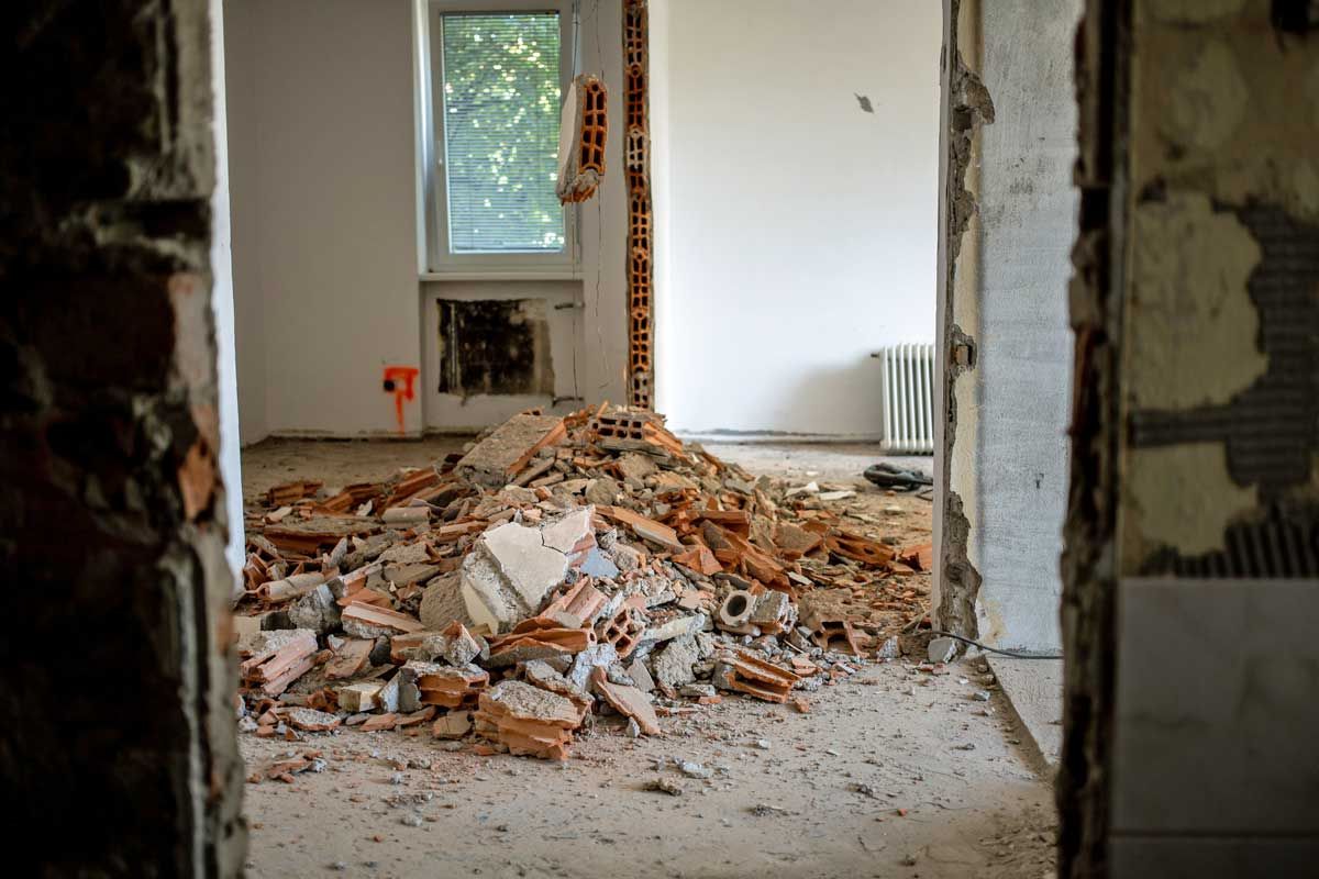 Room interior under renovation, rubble pile on floor, exposed brick and walls.