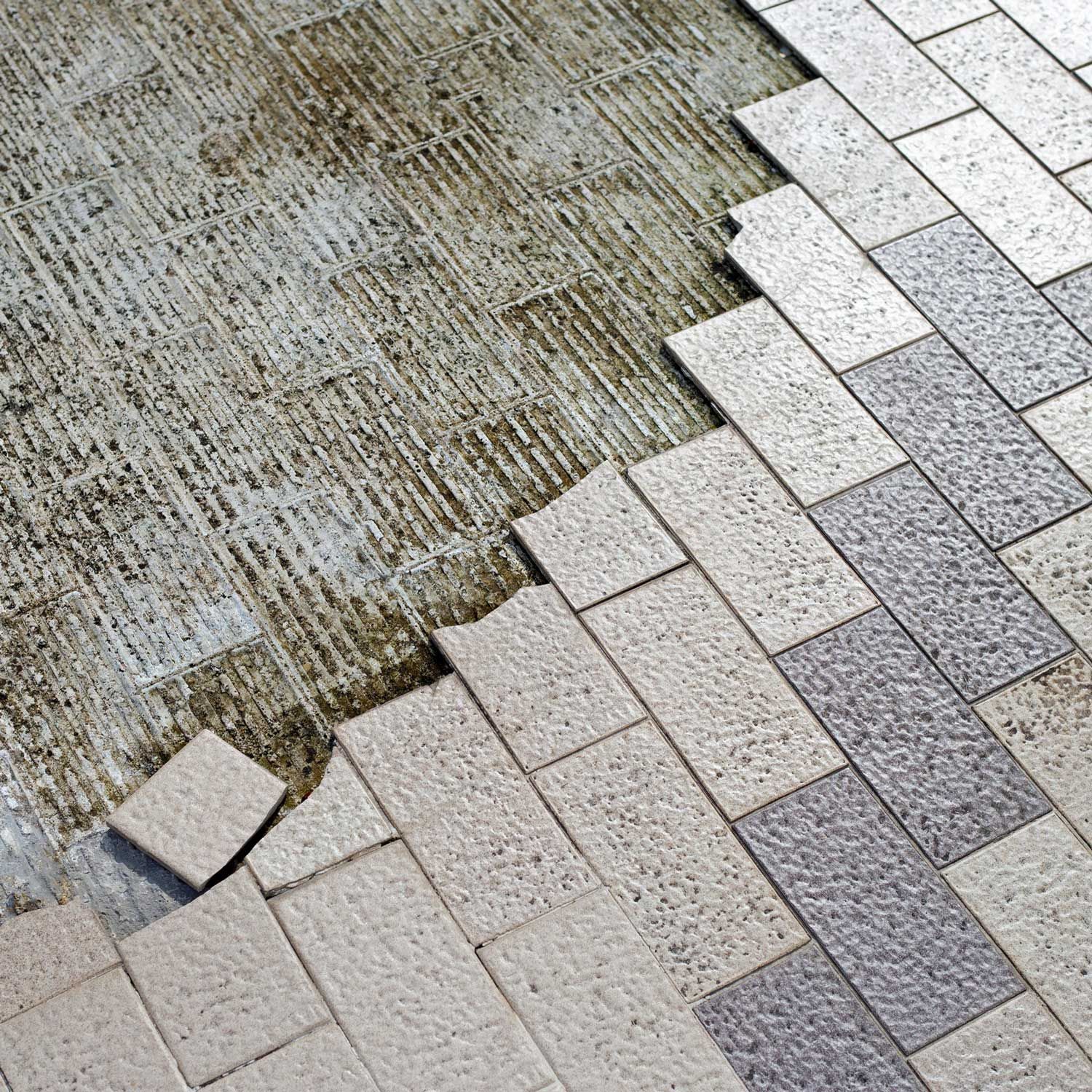 Partially laid light and dark gray rectangular paving stones, revealing an unpaved, textured surface.