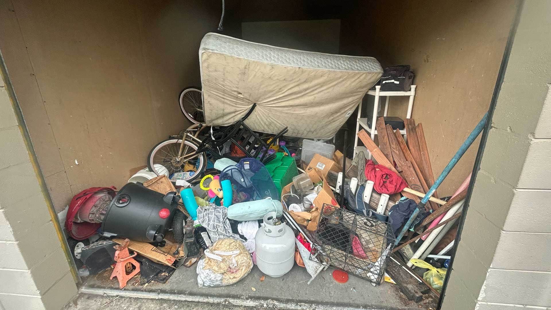 A storage unit filled with various items, including a mattress, a bicycle, and other clutter.
