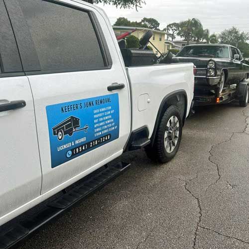 A white Keefer's truck is towing a black car on a trailer.