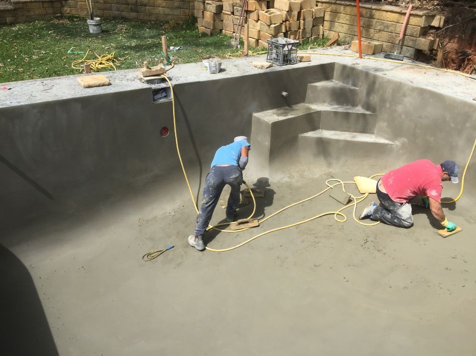 two men are working on a swimming pool .