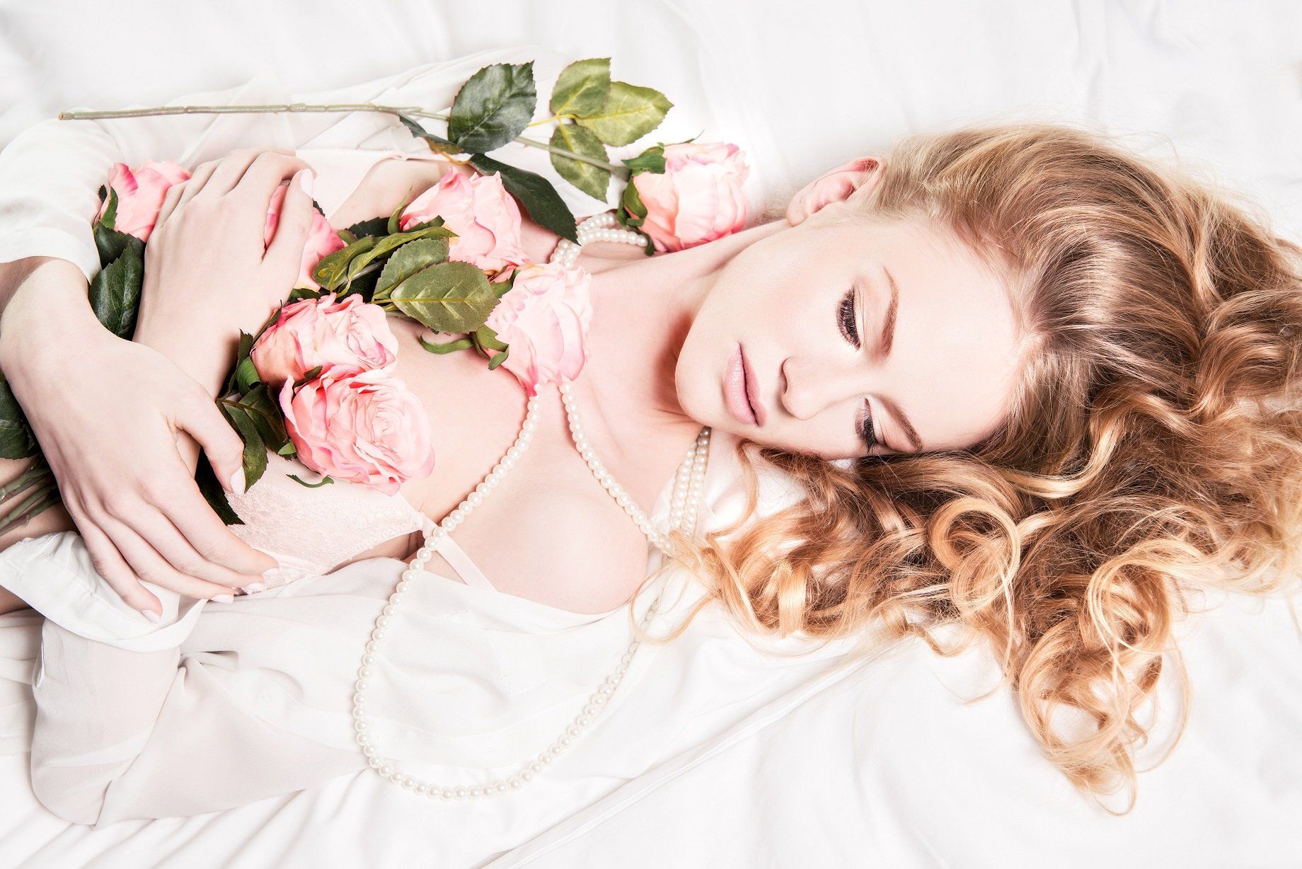 Eine Frau liegt auf einem Bett und hält einen Strauß rosa Rosen in der Hand.