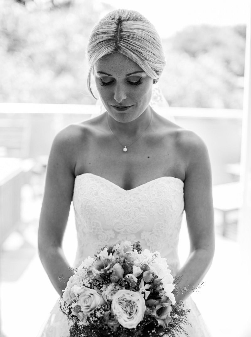 Ein Schwarzweißfoto einer Braut im Brautkleid, die einen Blumenstrauß hält.