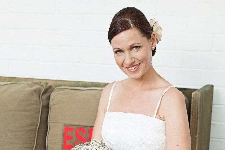 Eine Frau in einem weißen Kleid sitzt auf einem Sofa und hält einen Blumenstrauß in der Hand.