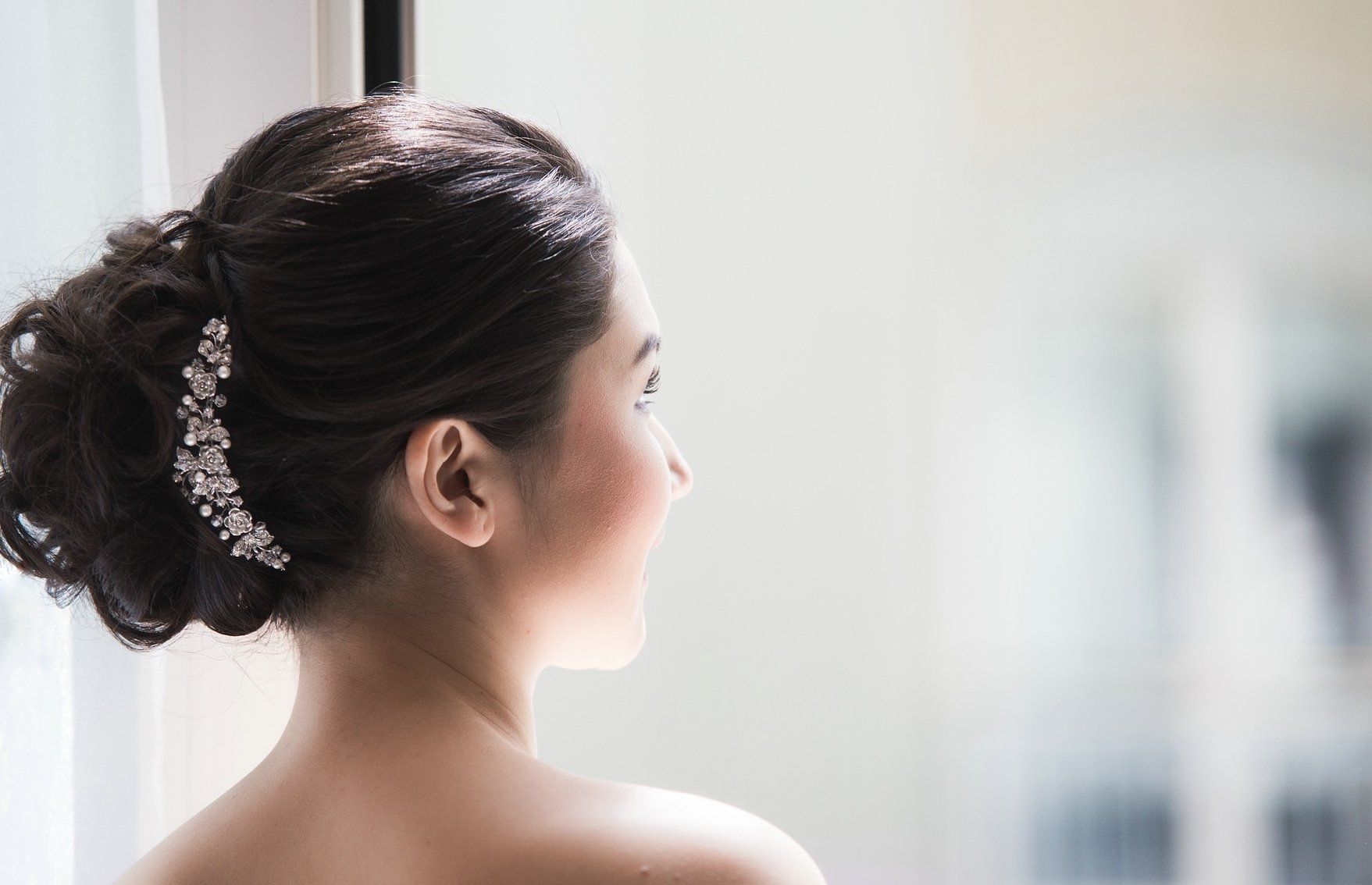 Eine Frau mit einem Dutt steht vor einem Fenster.