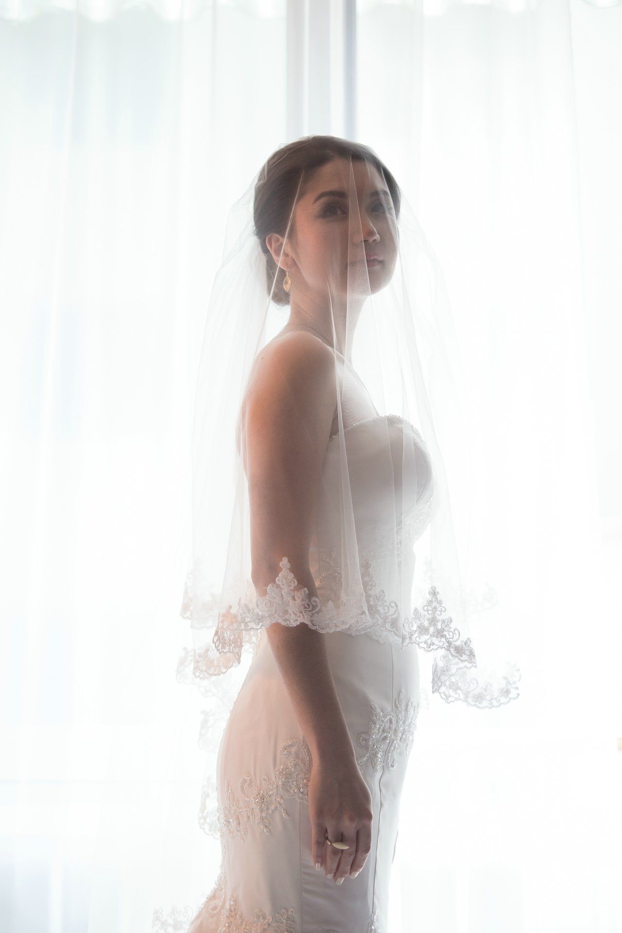 Eine Braut in einem Brautkleid und Schleier steht vor einem Fenster.