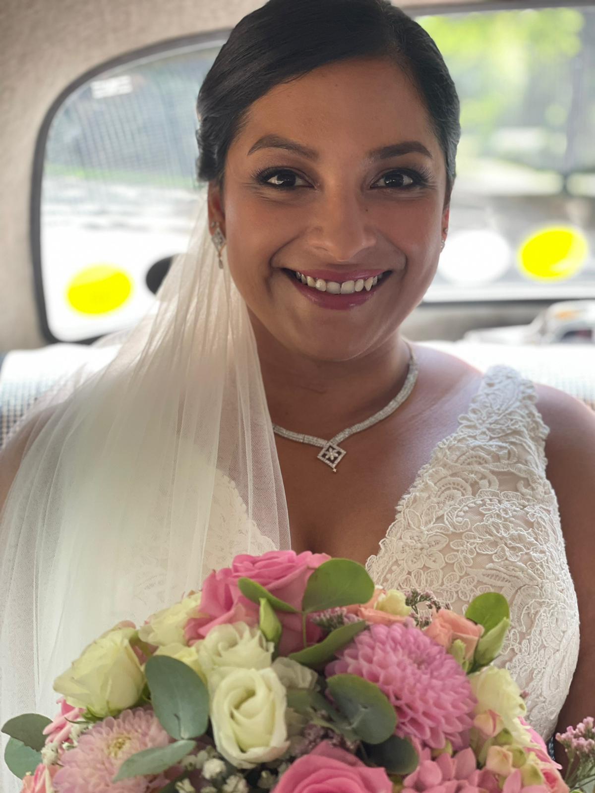 Die Braut lächelt und hält einen Strauß rosa und weißer Blumen in der Hand.