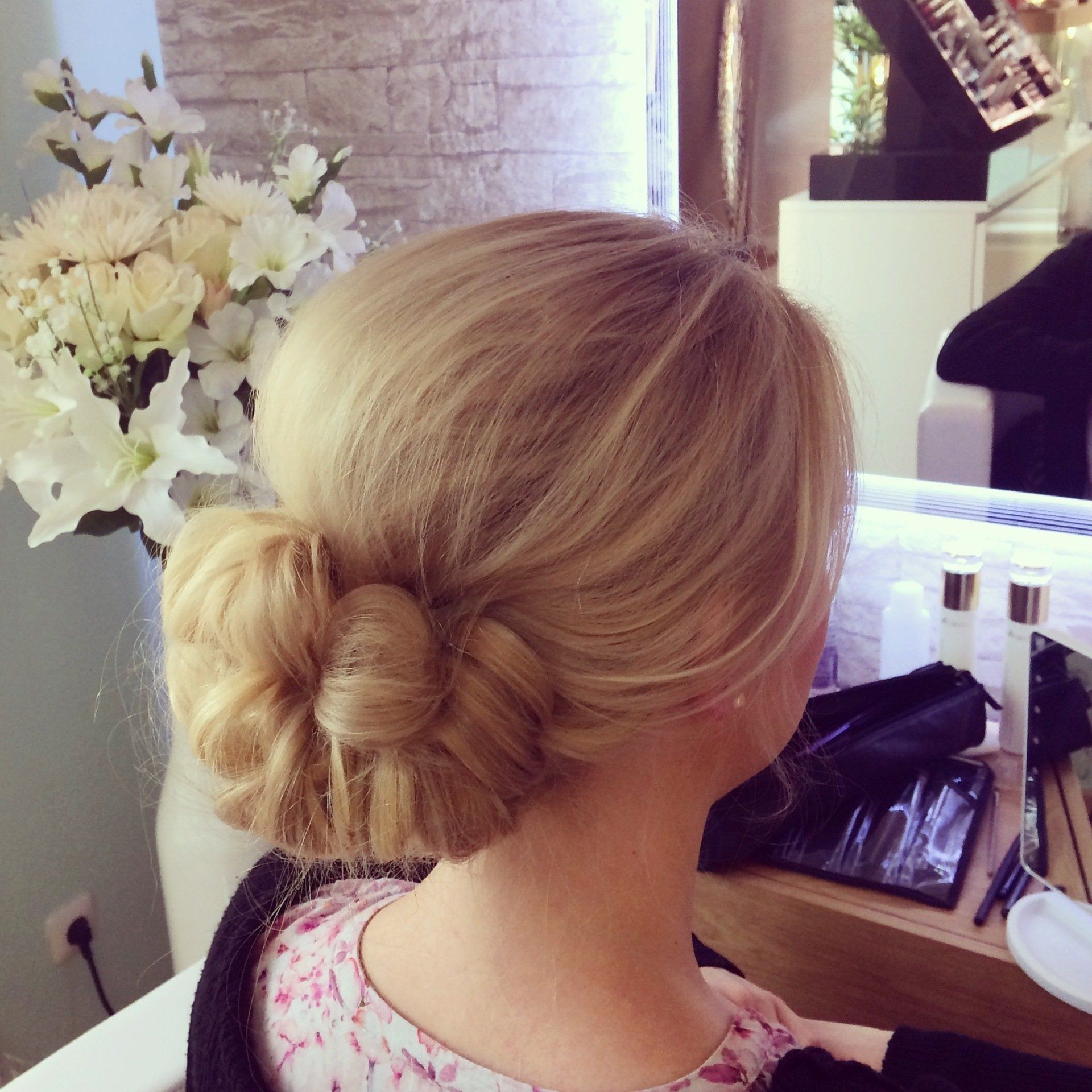 Eine Frau mit blonden Haaren in einem Dutt sitzt vor einem Spiegel