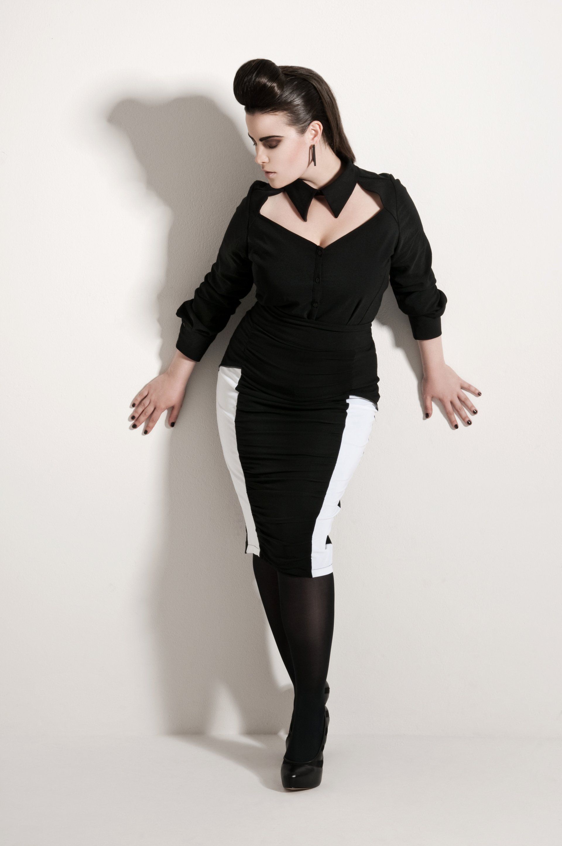 Eine Frau in einem schwarz-weißen Kleid lehnt an einer Wand.