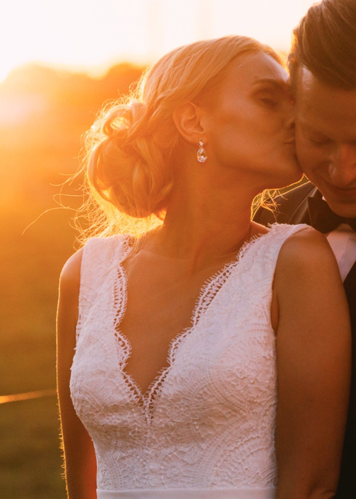 Eine Braut und ein Bräutigam küssen sich bei Sonnenuntergang auf einem Feld.