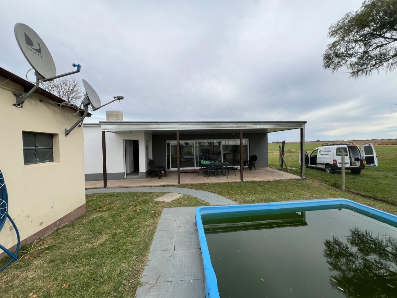 Patio trasero con una pequeña piscina, patio cubierto, casa, antena parabólica y una furgoneta 