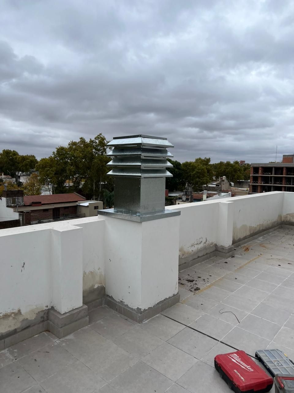 Terraza en la azotea con muros de parapeto blancos, chimenea de ventilación, cielo nublado 