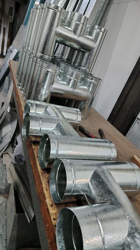 Tuberías y accesorios de conductos metálicos brillantes apilados en un taller o área de almacenamiento.