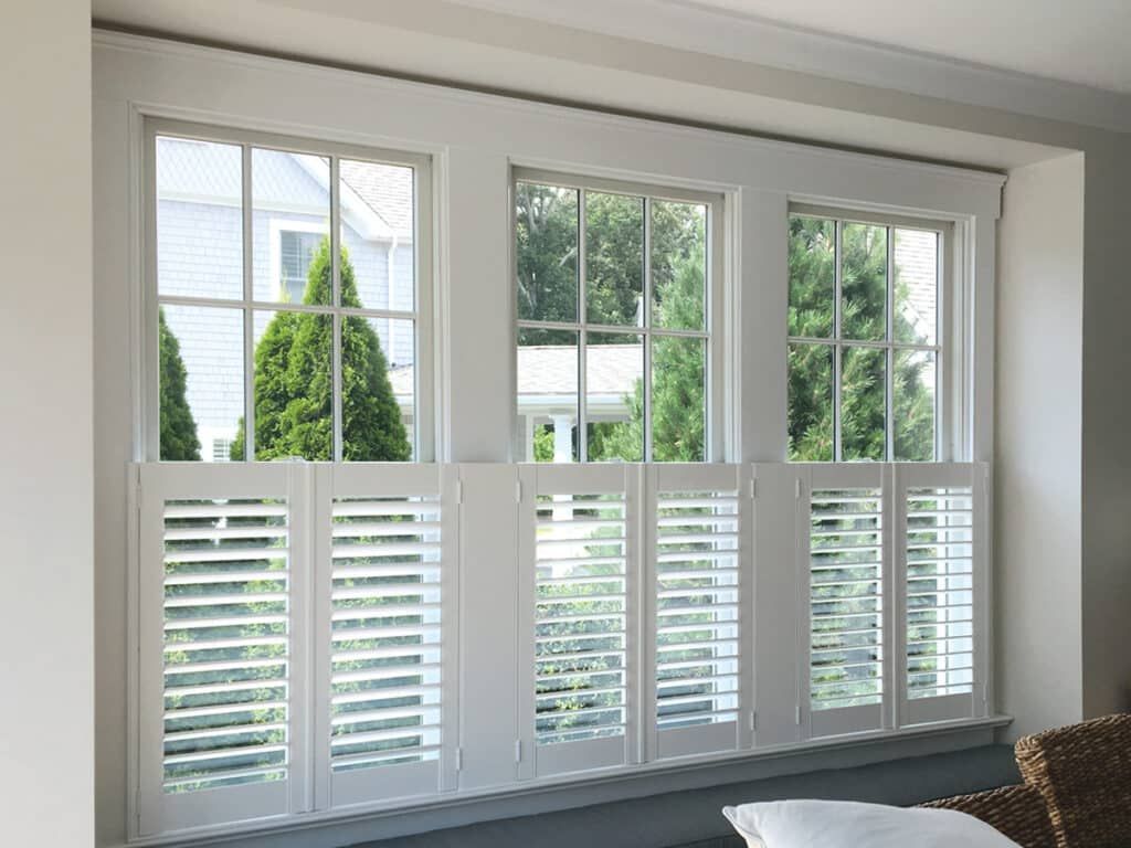 White shutters on three pane windows. Trees and a house visible through the glass.