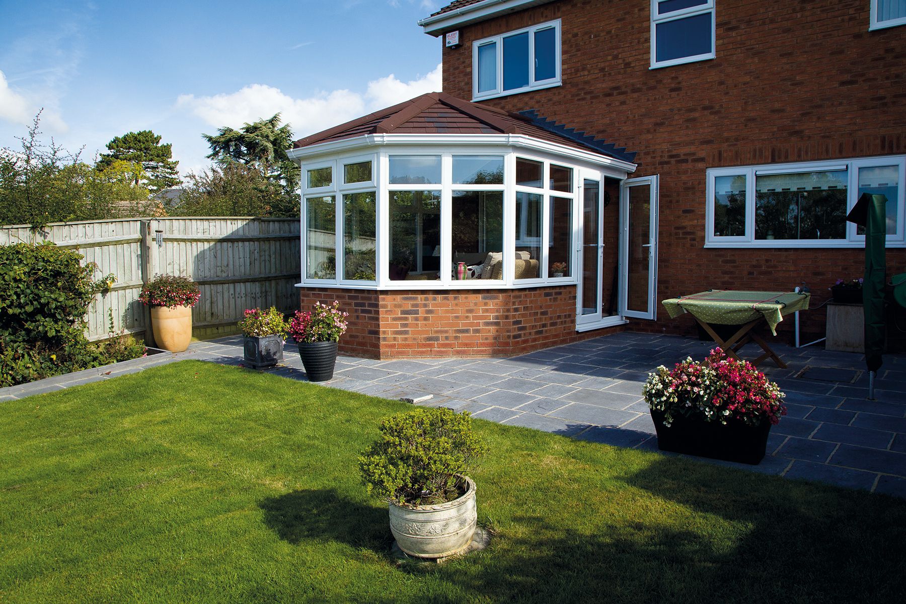 Brick home with a sunroom and patio in a backyard with a green lawn.