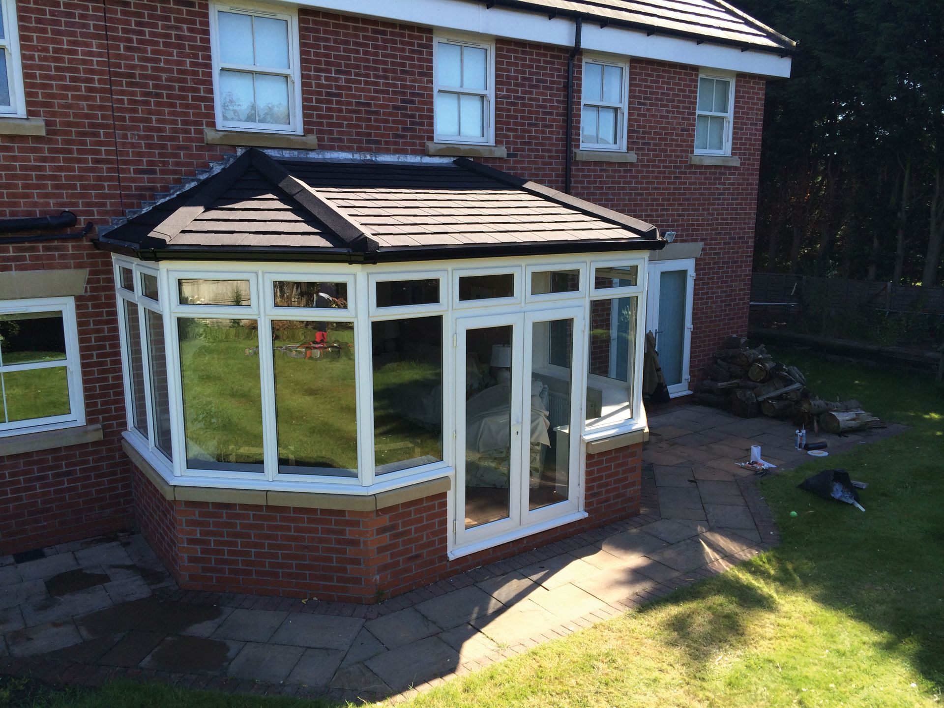 Brick house with white-framed conservatory and dark roof. Door open onto patio, lawn in foreground.