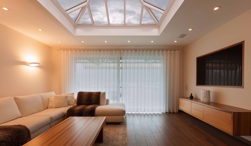 Living room with a skylight, couch, curtains, TV, and wooden floors.