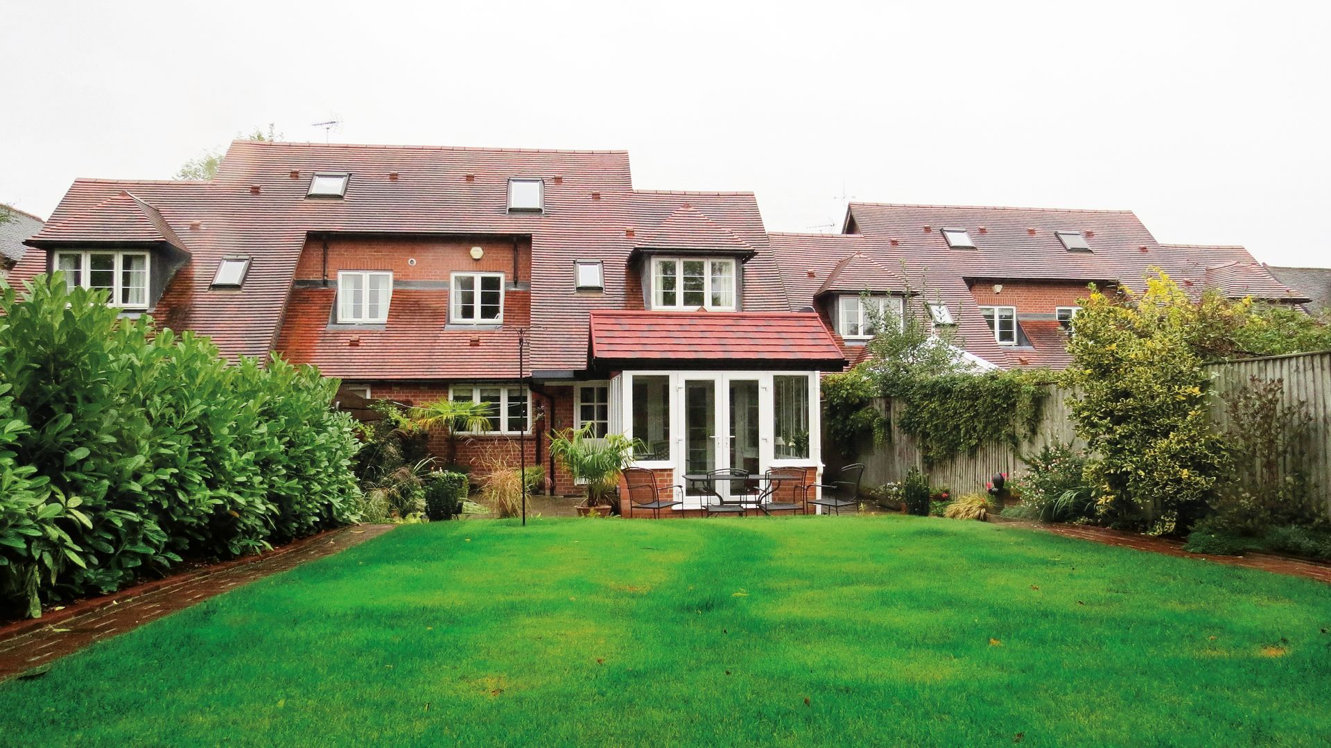 House with red tiled roof, brick walls, surrounded by a green lawn and hedges.