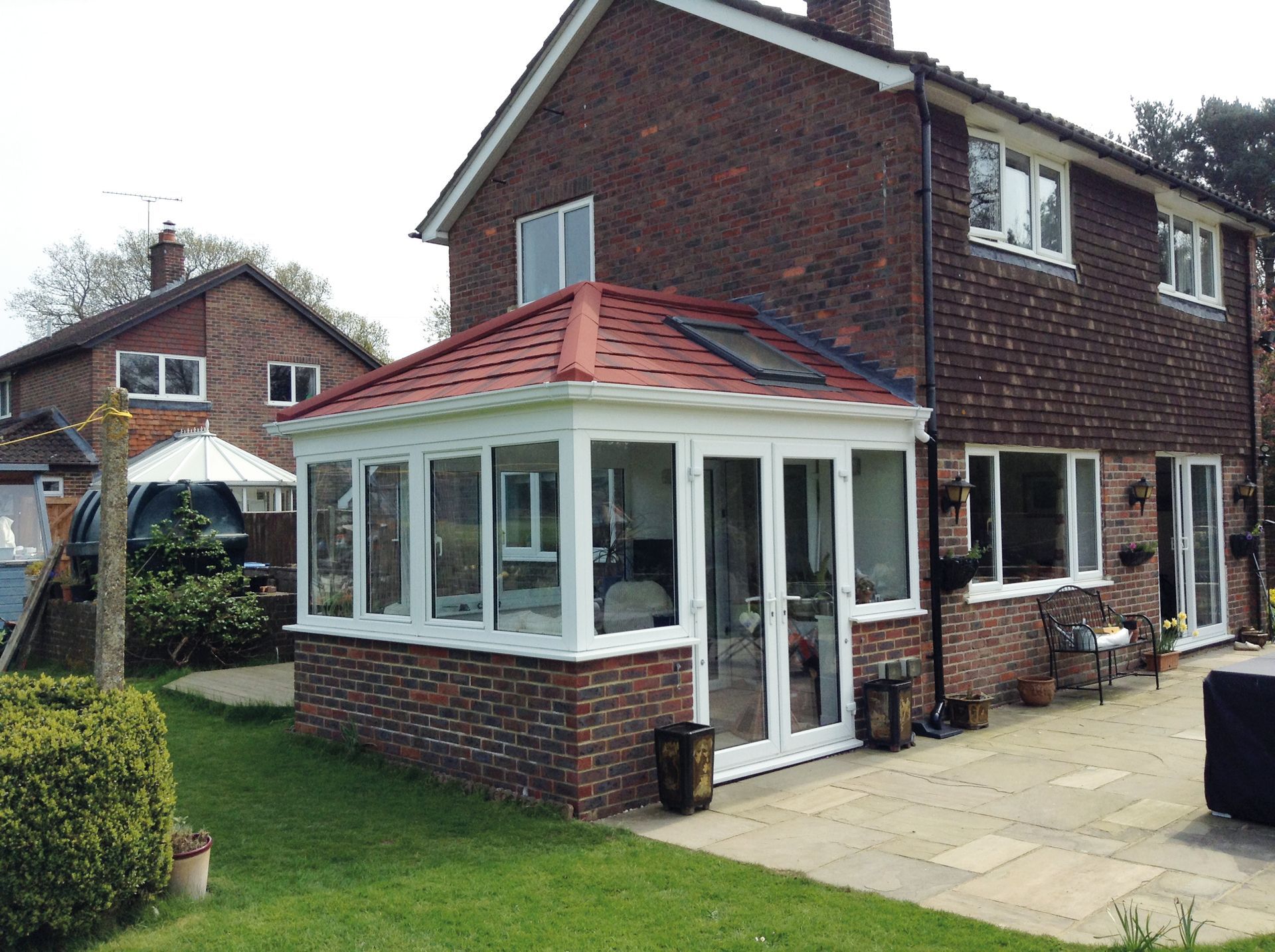 Brick house with a conservatory featuring white frames, red roof tiles, and a patio.