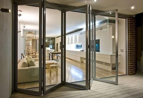 Folding glass doors open to reveal a modern living space with white walls, furniture, and hardwood floors.
