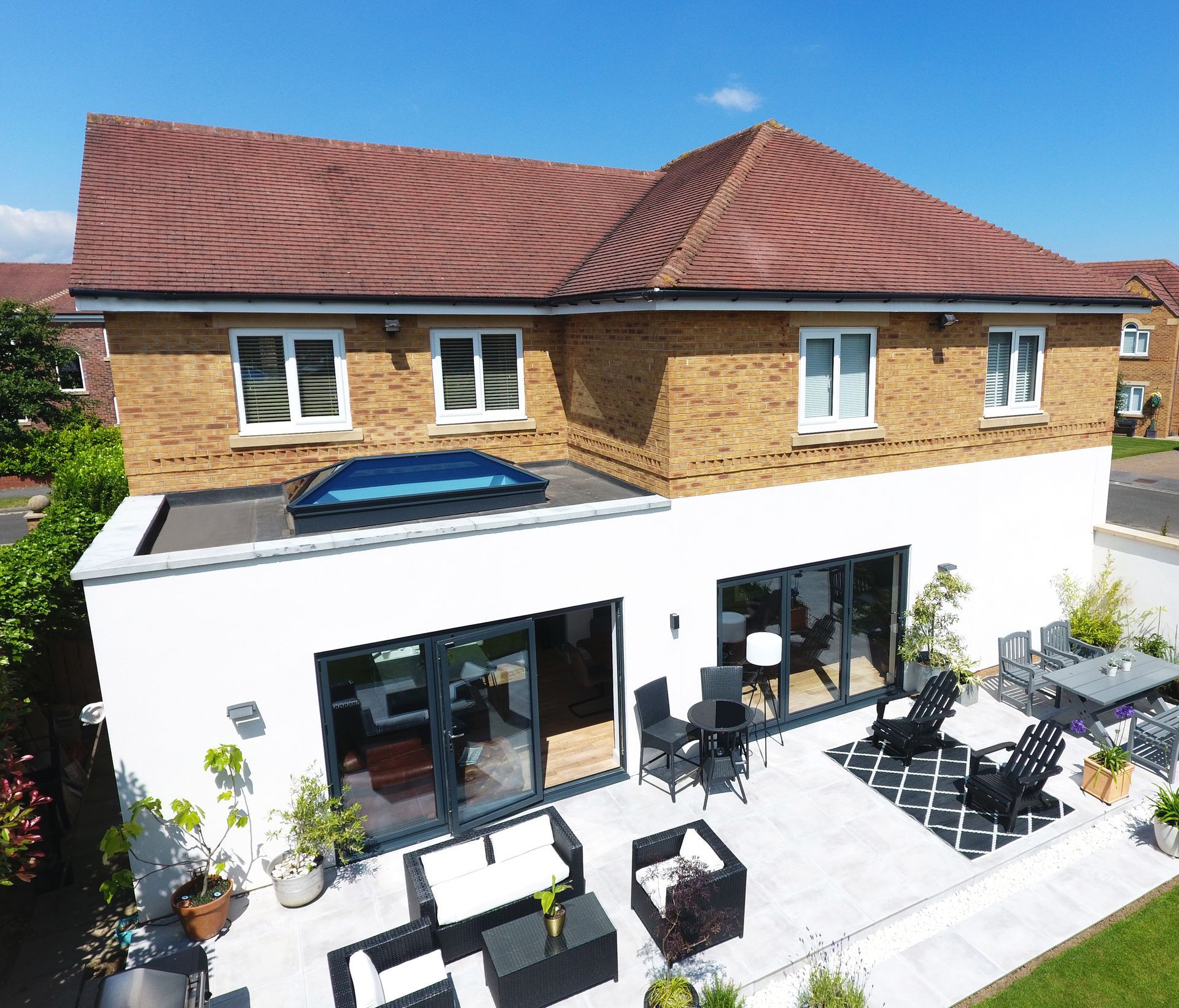 Two-story house with a white extension, a patio, and outdoor seating under a blue sky.